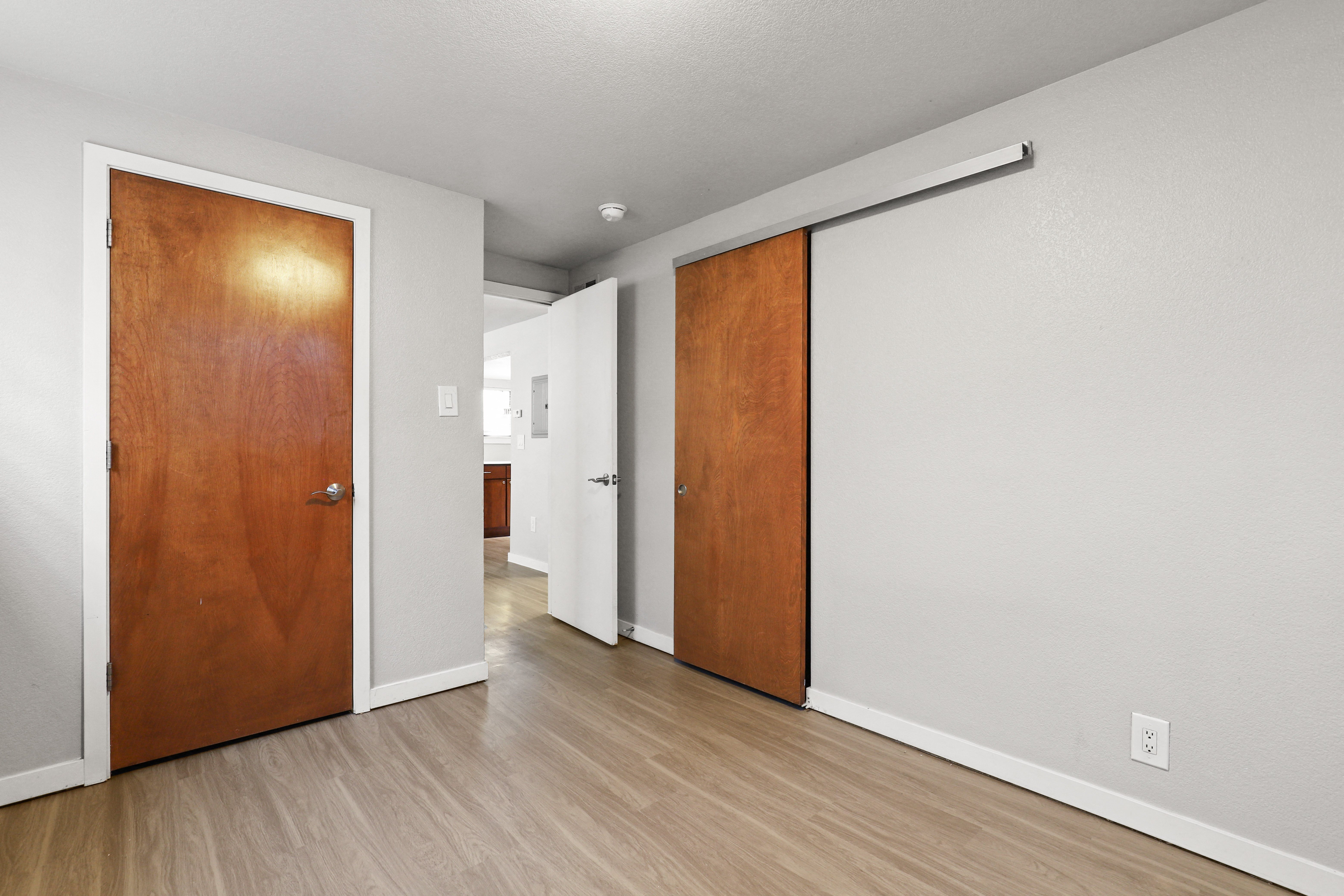 an empty living room with a wooden door and a hallway to a bedroom